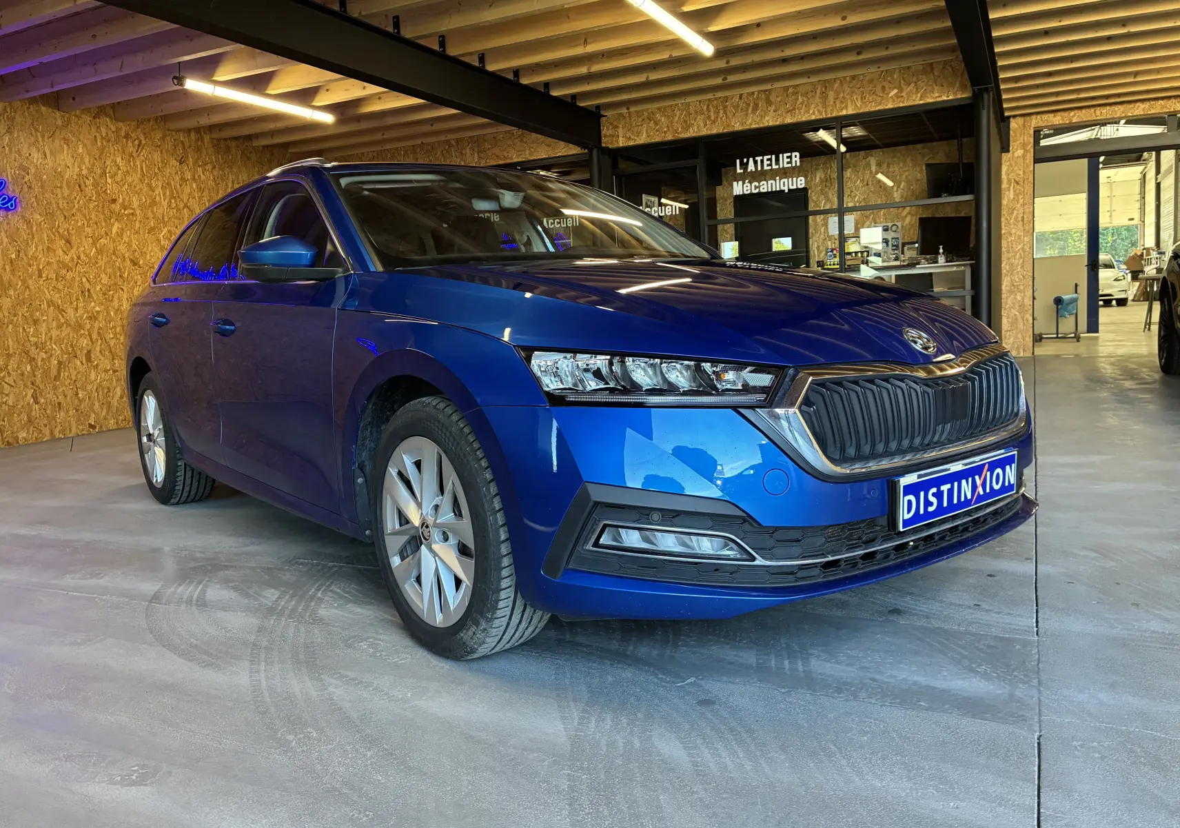 Vue 3/4 avant droite d'une Skoda Octavia Combi 2024 bleu, avec calandre noire et phares LED, stationnée en intérieur.