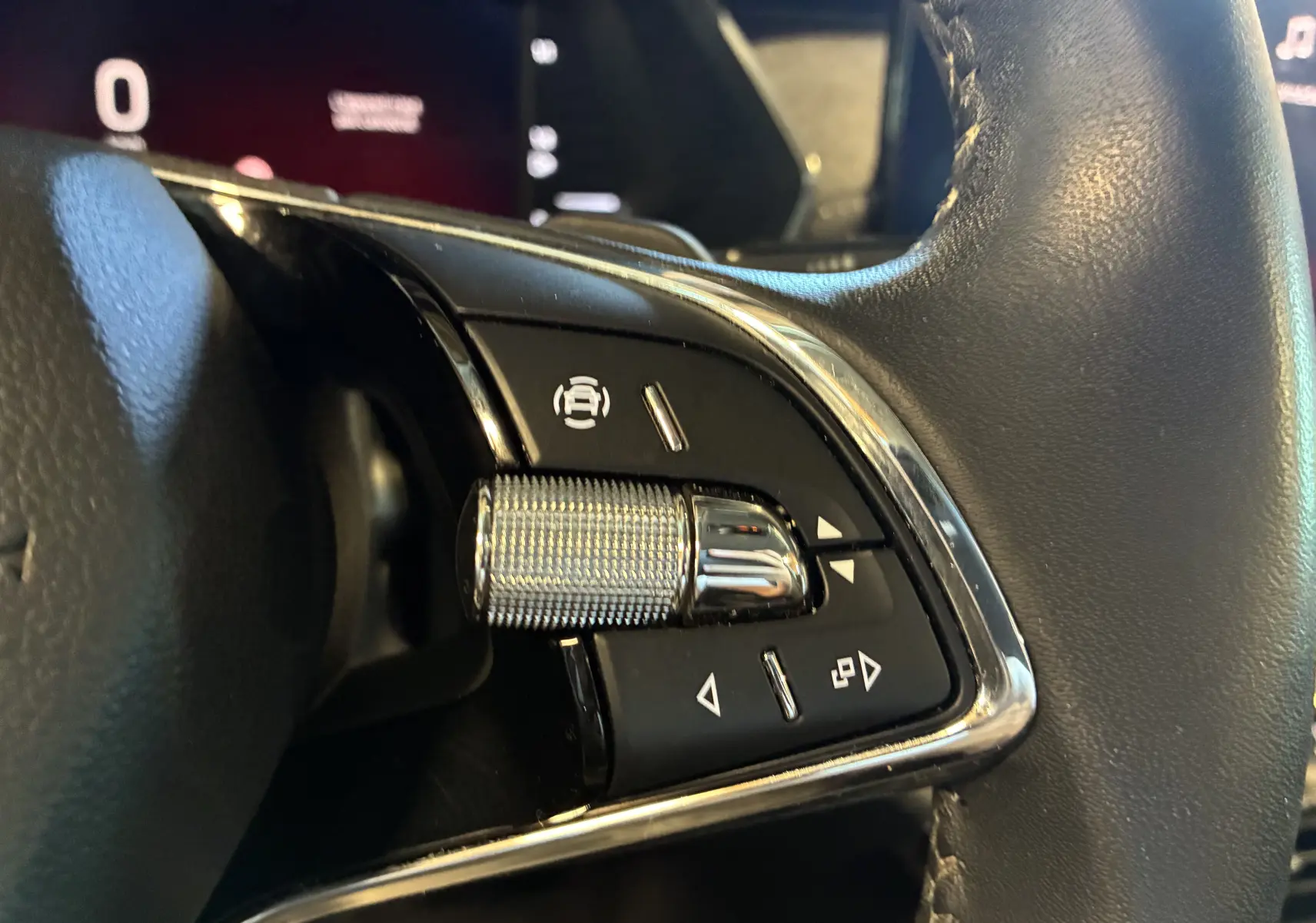 Gros plan sur les commandes multifonctions en métal et plastique noir du volant côté gauche d'une Skoda Octavia Combi bleu 2024.