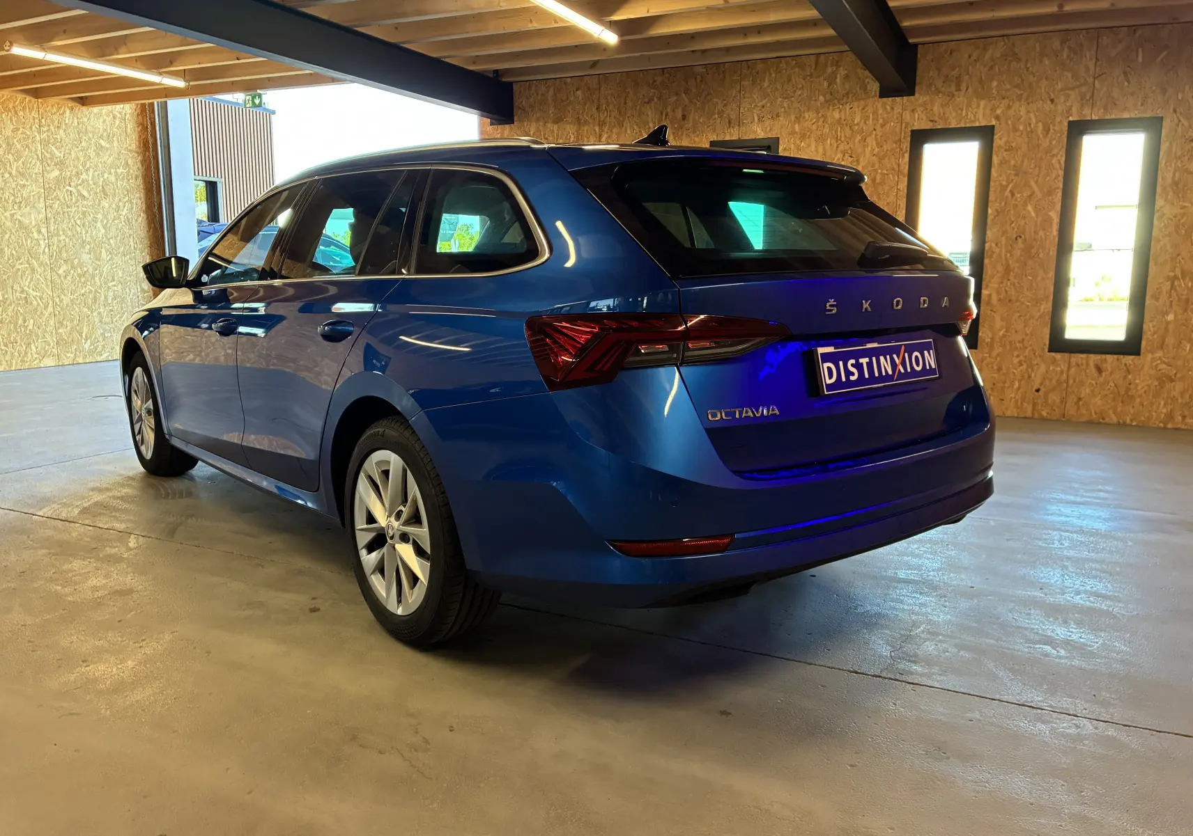 Vue 3/4 arrière droite d'une Skoda Octavia Combi bleu 2024, avec feux arrière LED et finition Style dans un garage.