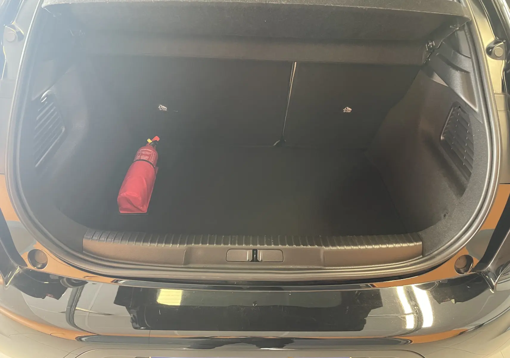 Coffre ouvert d'une DS3 Crossback Perla Nera 2024, vue arrière, avec extincteur rouge posé à gauche dans un espace noir épuré.