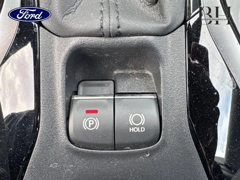 Gros plan sur les commandes de frein à main électronique et maintien automatique sur console noire brillante d'une Toyota Corolla gris Manhattan.