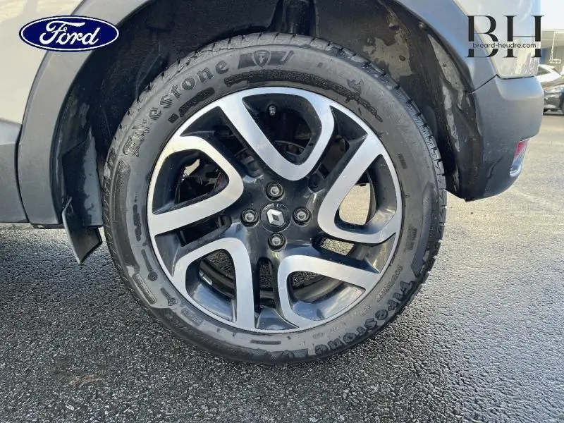 Gros plan sur la jante alu noire et argentée avec logo Renault du Renault Captur beige cendré, toit noir étoilé.