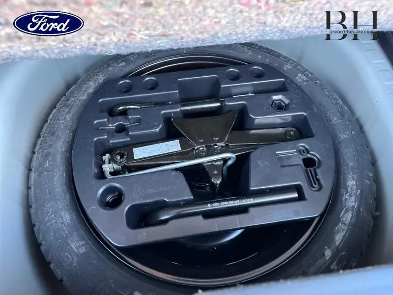 Gros plan sur la roue de secours avec outils de changement dans le coffre d'une Renault Captur beige cendré toit noir.