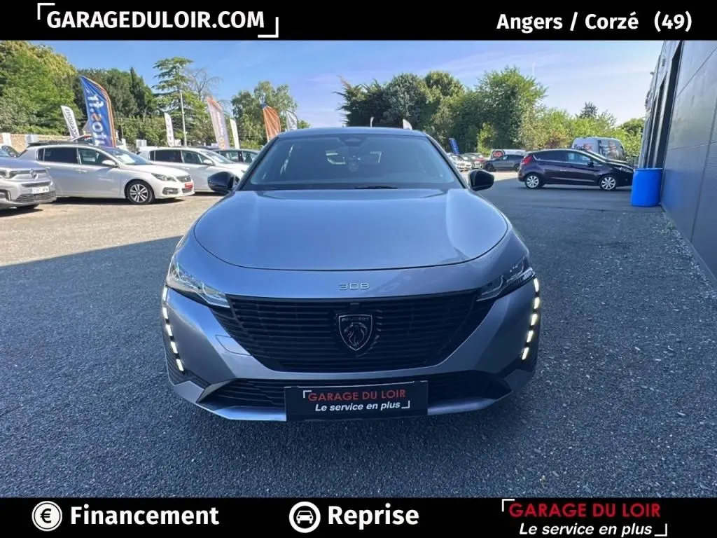 Vue avant d'une Peugeot 308 gris clair 2023 avec calandre noire et feux LED verticaux allumés.
