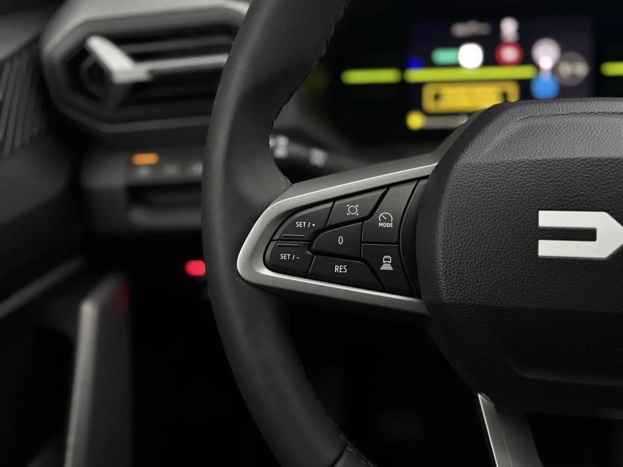 Gros plan sur le volant noir du Dacia Duster 2026 avec commandes multifonctions et tableau de bord digital flou en arrière-plan.