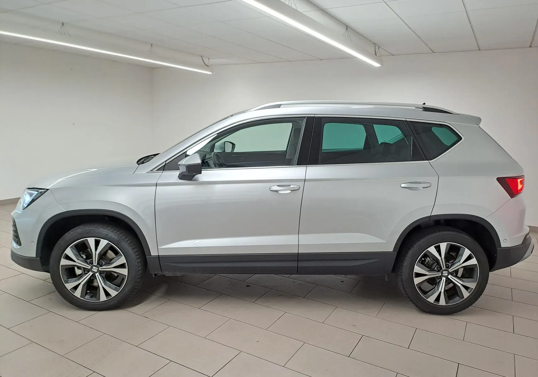 Vue de profil droit du SUV SEAT Ateca 2025 en argent métallisé avec jantes alliage 18 pouces dans un intérieur neutre.
