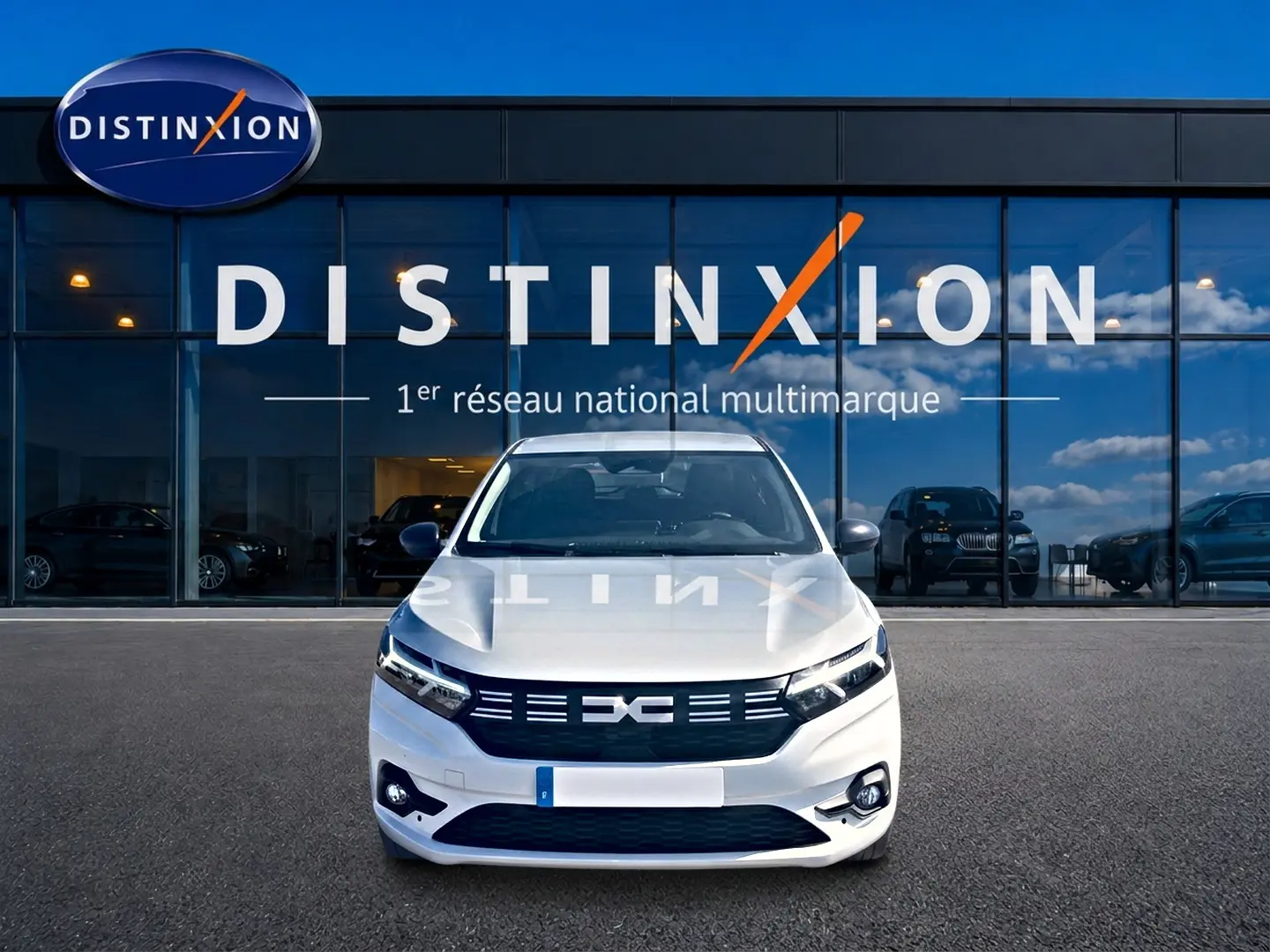 Vue frontale d'une Dacia Sandero blanche 2025 garée devant une vitrine avec logo Distinxion.