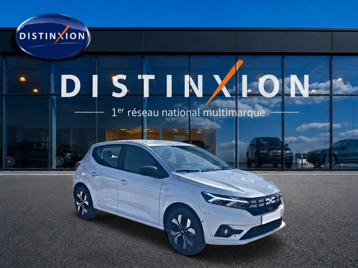 Vue 3/4 avant gauche d'une Dacia Sandero blanche 2025 avec jantes alu et vitres teintées devant un showroom Distinxion.