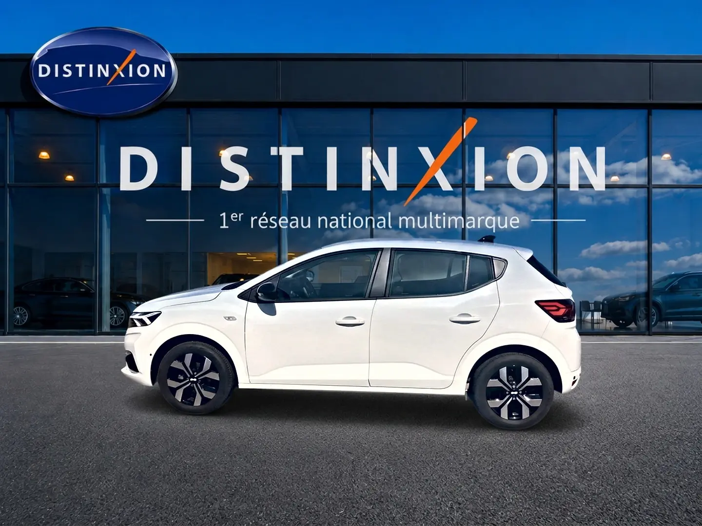 Profil droit d'une Dacia Sandero blanche 2025 garée devant une vitrine avec logo Distinxion.