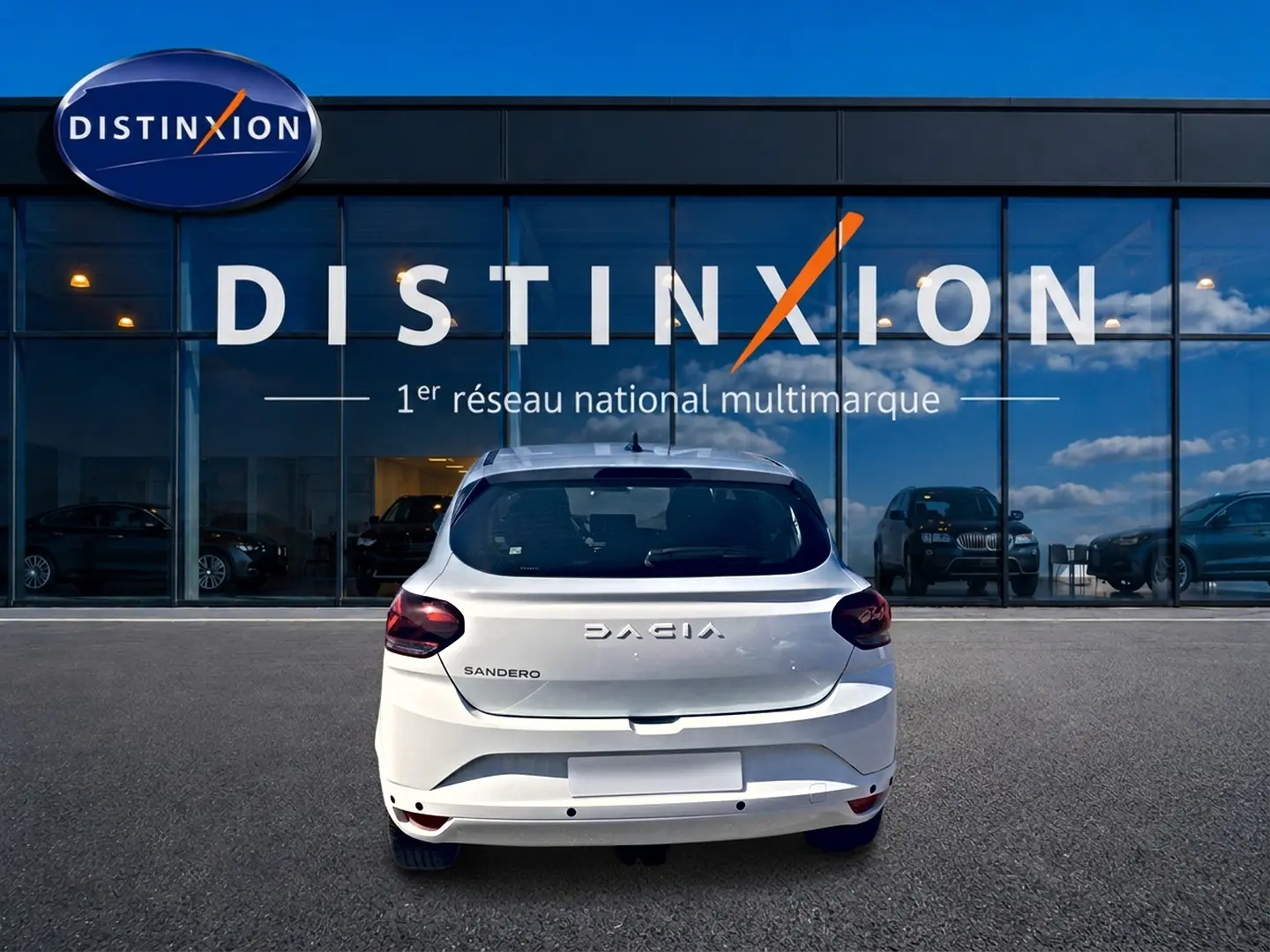 Vue arrière d'une Dacia Sandero blanche 2025 garée devant une vitrine avec logo Distinxion.