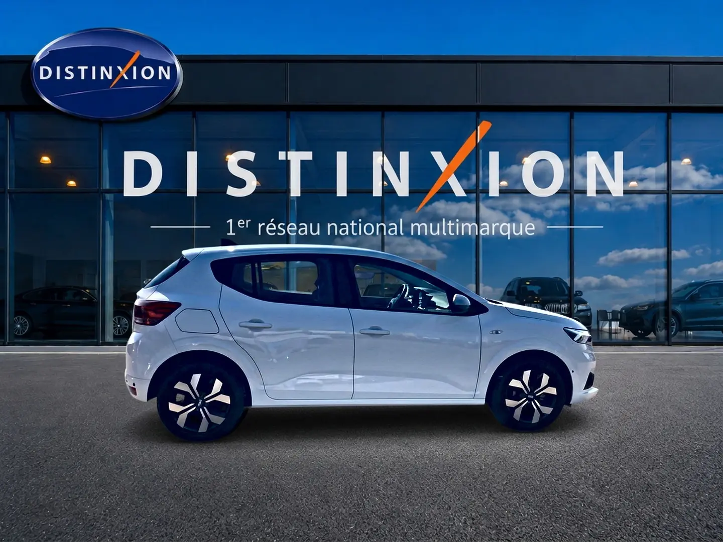 Profil côté gauche d'une Dacia Sandero blanche 2025 stationnée devant une vitrine Distinxion.