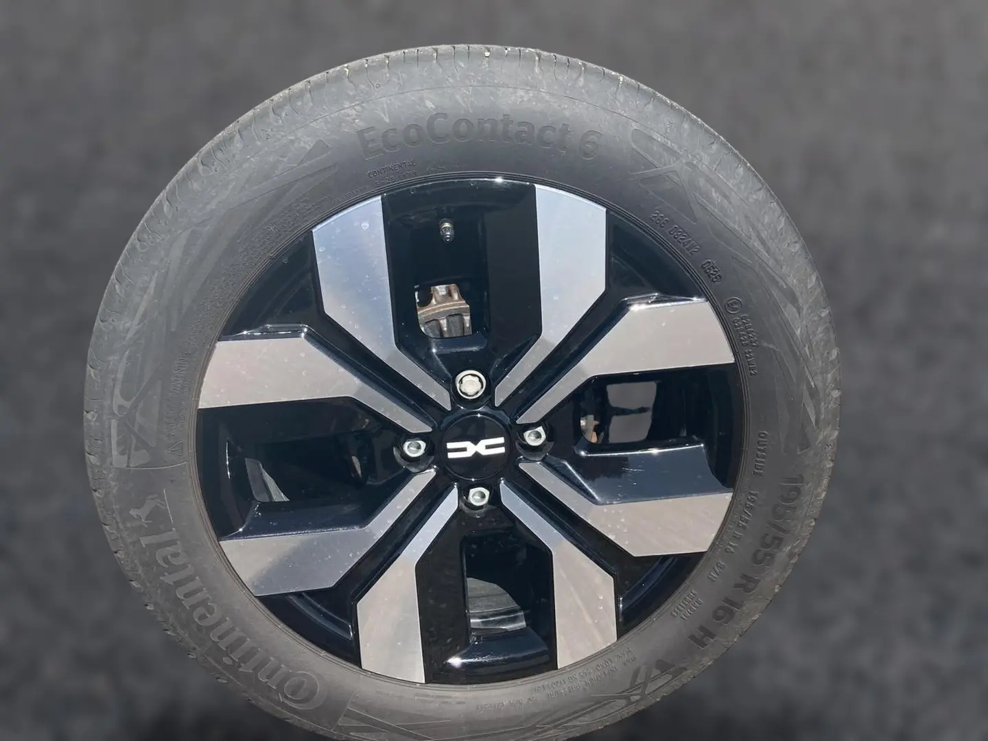 Gros plan sur la jante alu noire et argentée d'une Dacia Sandero blanche, mettant en valeur le logo central.