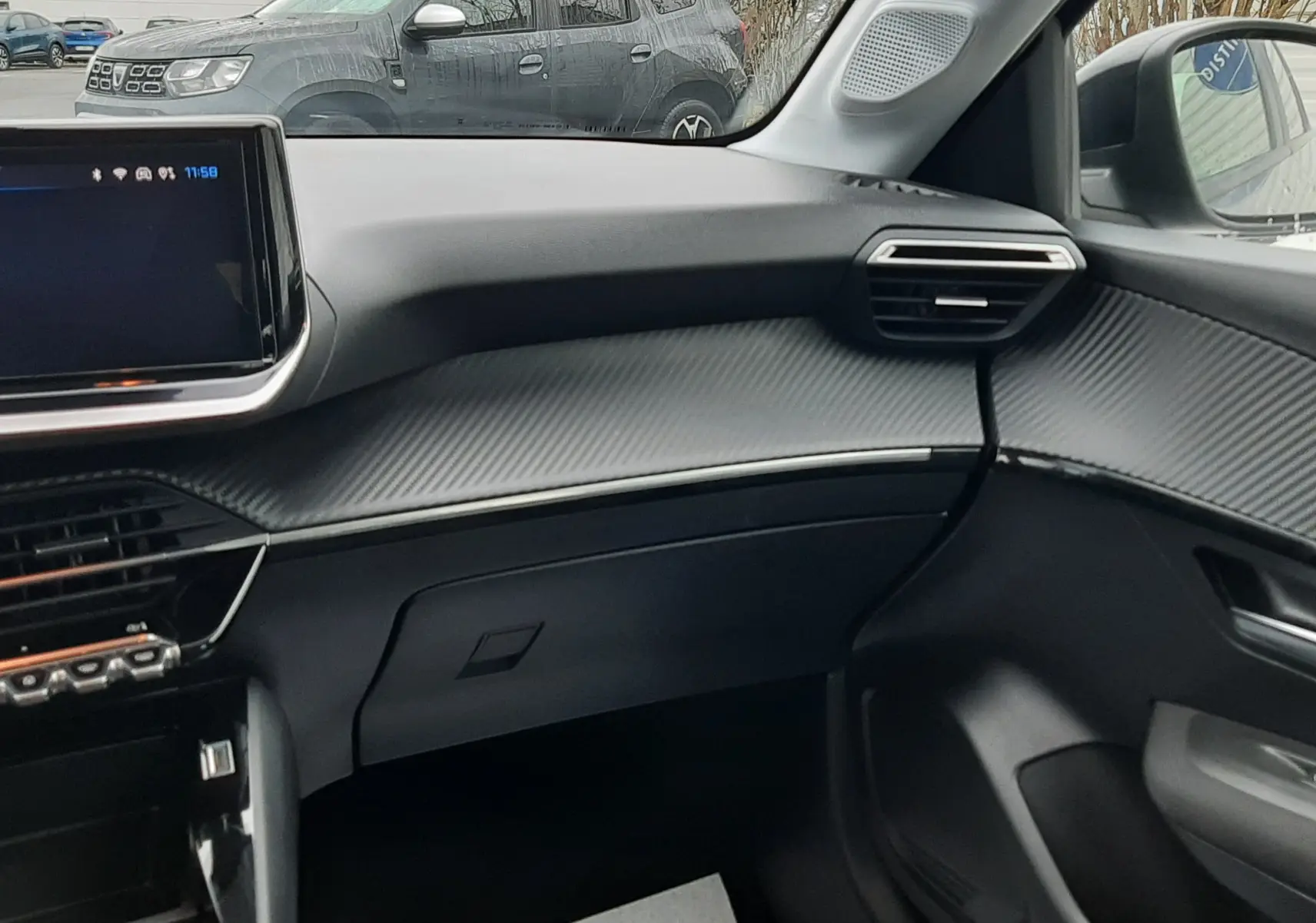 Vue intérieure côté passager de la Peugeot 208 2024, tableau de bord gris avec finition texturée et écran tactile.