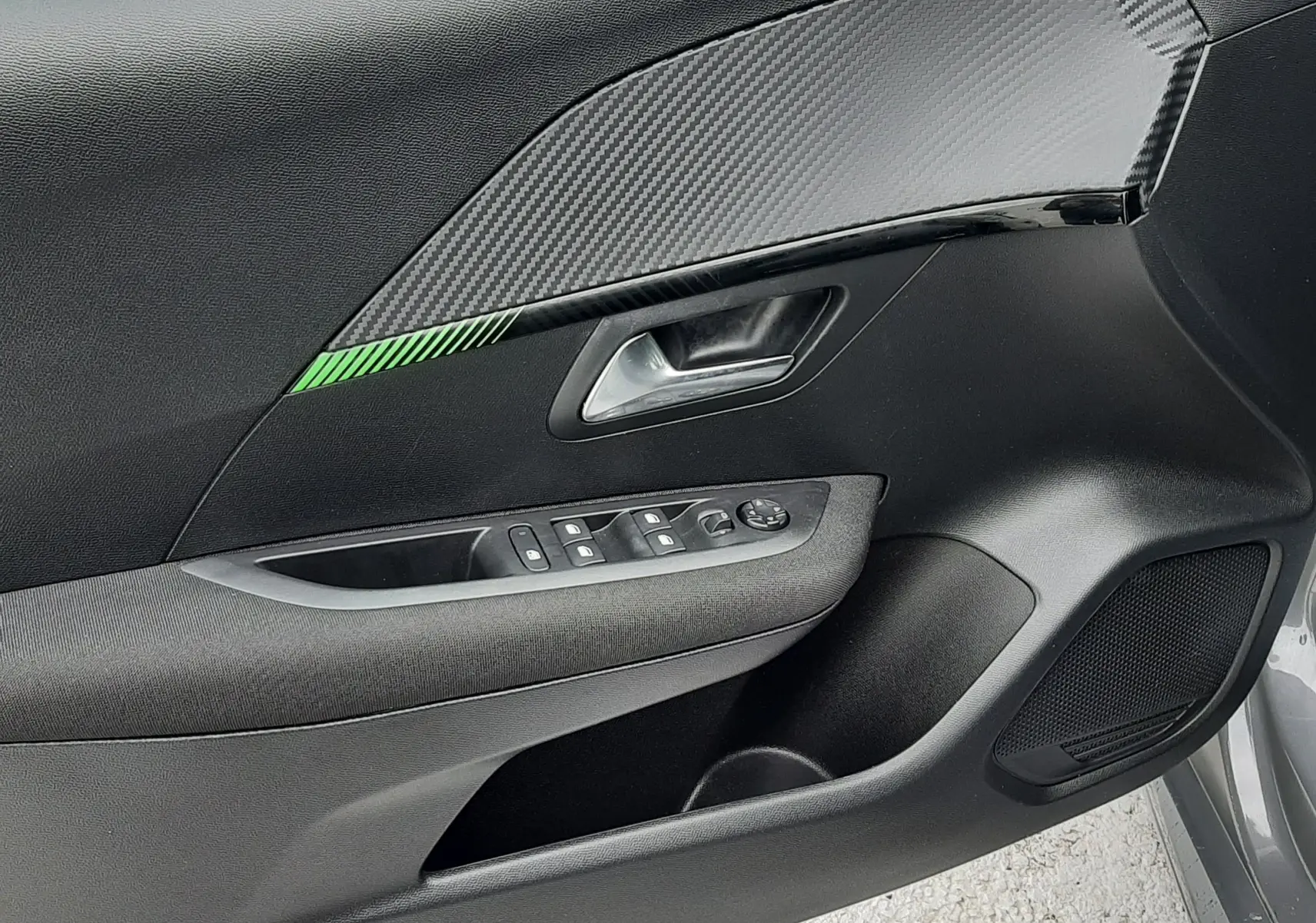 Détail de la porte avant gauche de la Peugeot 208 2024 gris selenium, avec insert décor carbone et commandes des vitres.