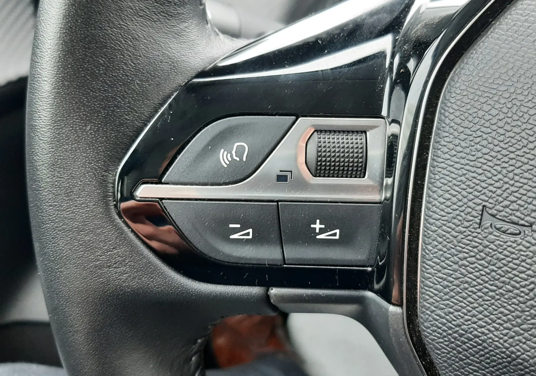 Gros plan sur les commandes gauche du volant noir d’une Peugeot 208 2024, avec boutons de volume et commande vocale.