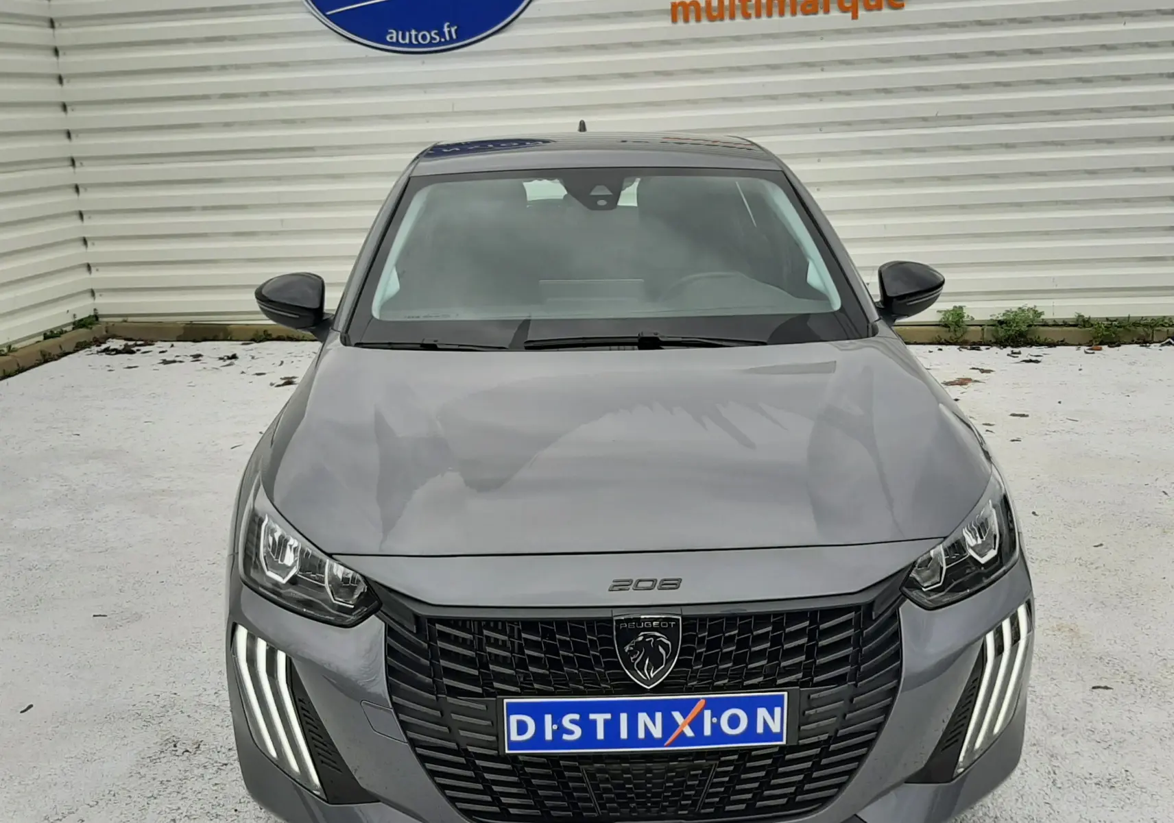 Peugeot 208 gris sélénium vue de face, avec calandre noire et feux LED verticaux allumés.