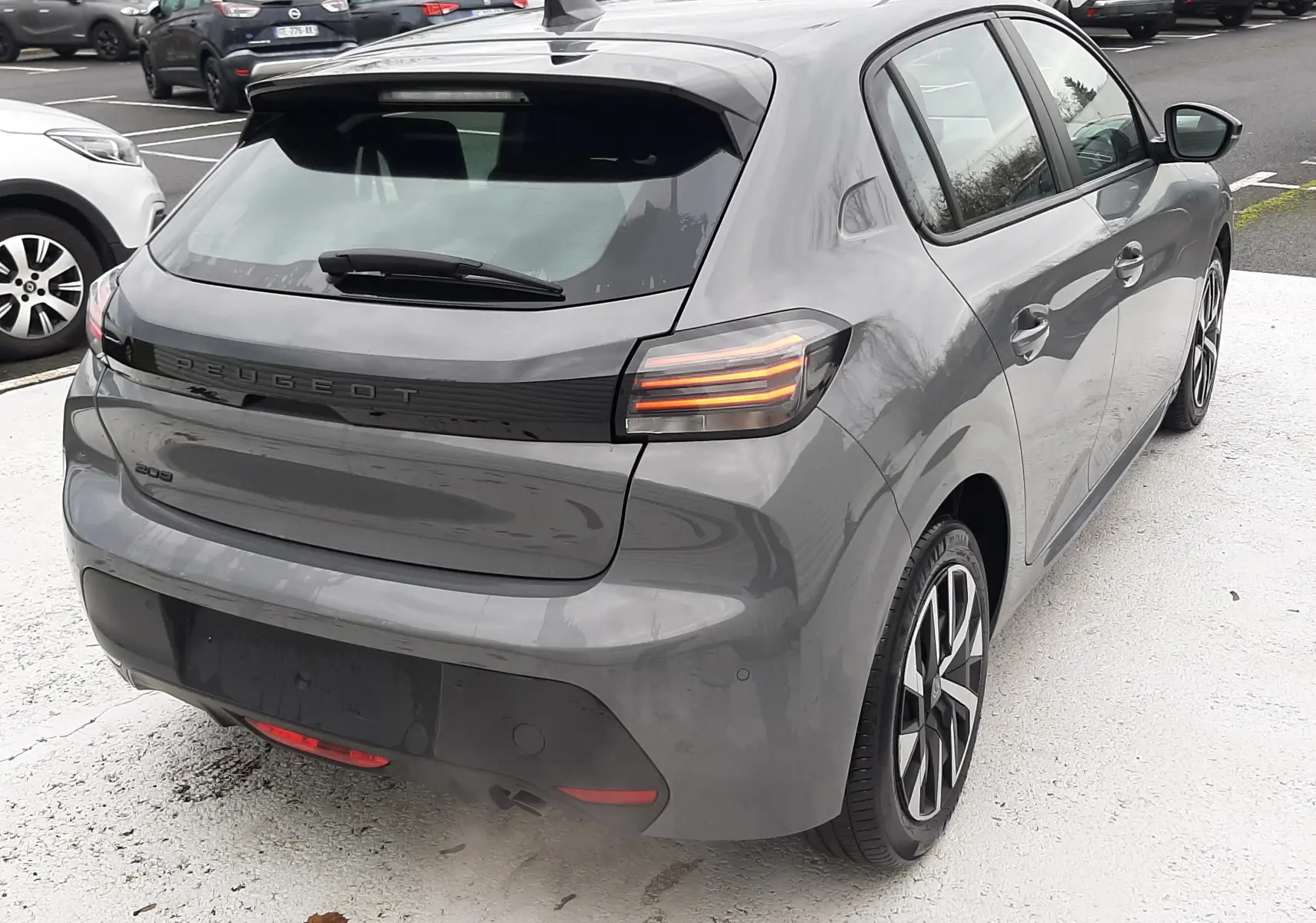 Vue 3/4 arrière droite d'une Peugeot 208 gris selenium 2024 avec feux arrière LED et jantes alliage distinctives.