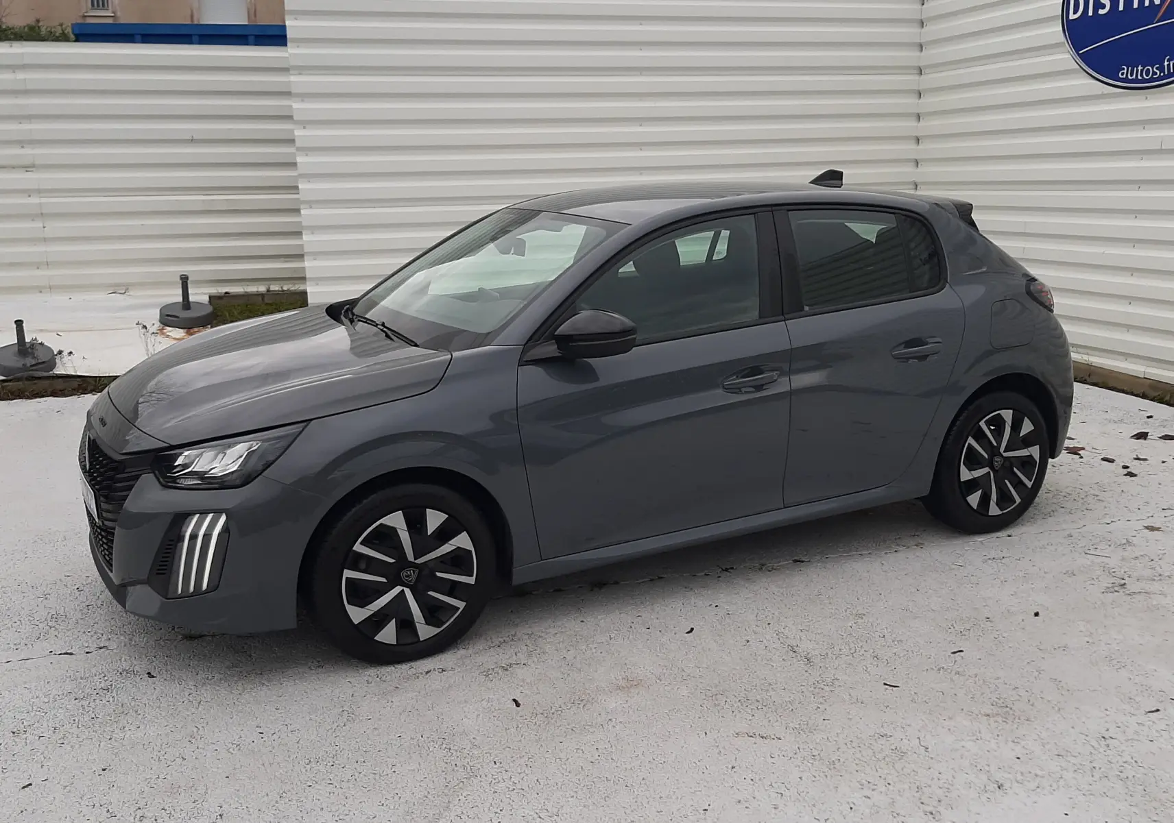 Peugeot 208 gris sélénium vue de profil côté gauche, avec feux LED verticaux distinctifs et jantes noires.