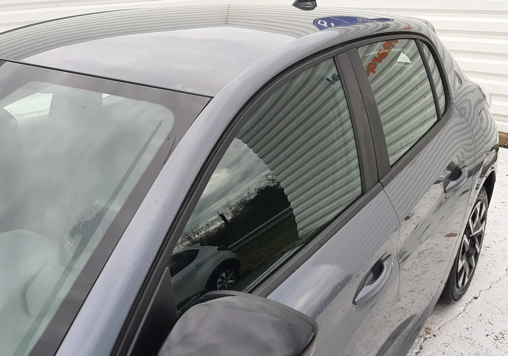 Vue 3/4 arrière côté gauche d'une Peugeot 208 gris selenium 2024 avec rétroviseur noir et vitres teintées.