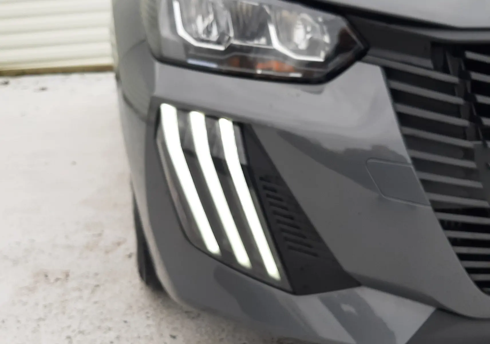 Gros plan sur l'avant droit gris sélénite du Peugeot 208 2024, mettant en valeur ses feux LED distinctifs en forme de griffes.
