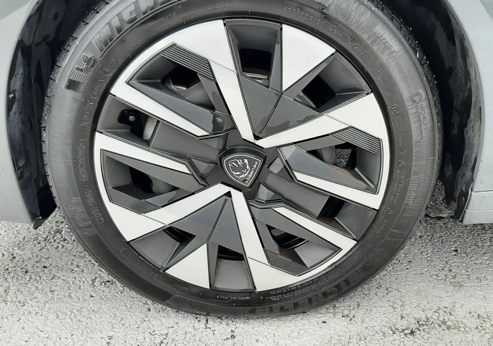 Gros plan sur la roue avant droite d'une Peugeot 208 2024 gris selenium avec jante alliage au design géométrique noir et argent.