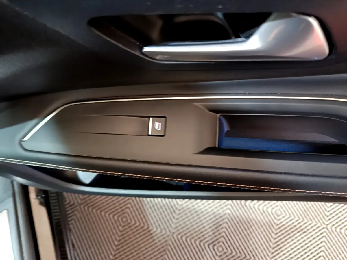 Poignée de porte intérieure côté gauche du Peugeot 3008 noir 2023 avec bouton de lève-vitre et surpiqûres contrastées.