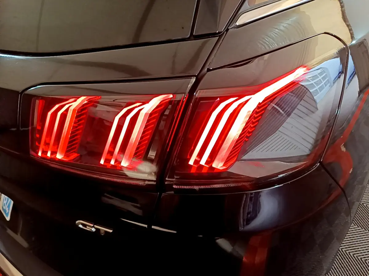 Gros plan sur les feux arrière allumés côté gauche d'un Peugeot 3008 GT noir 2023, avec logo GT visible.
