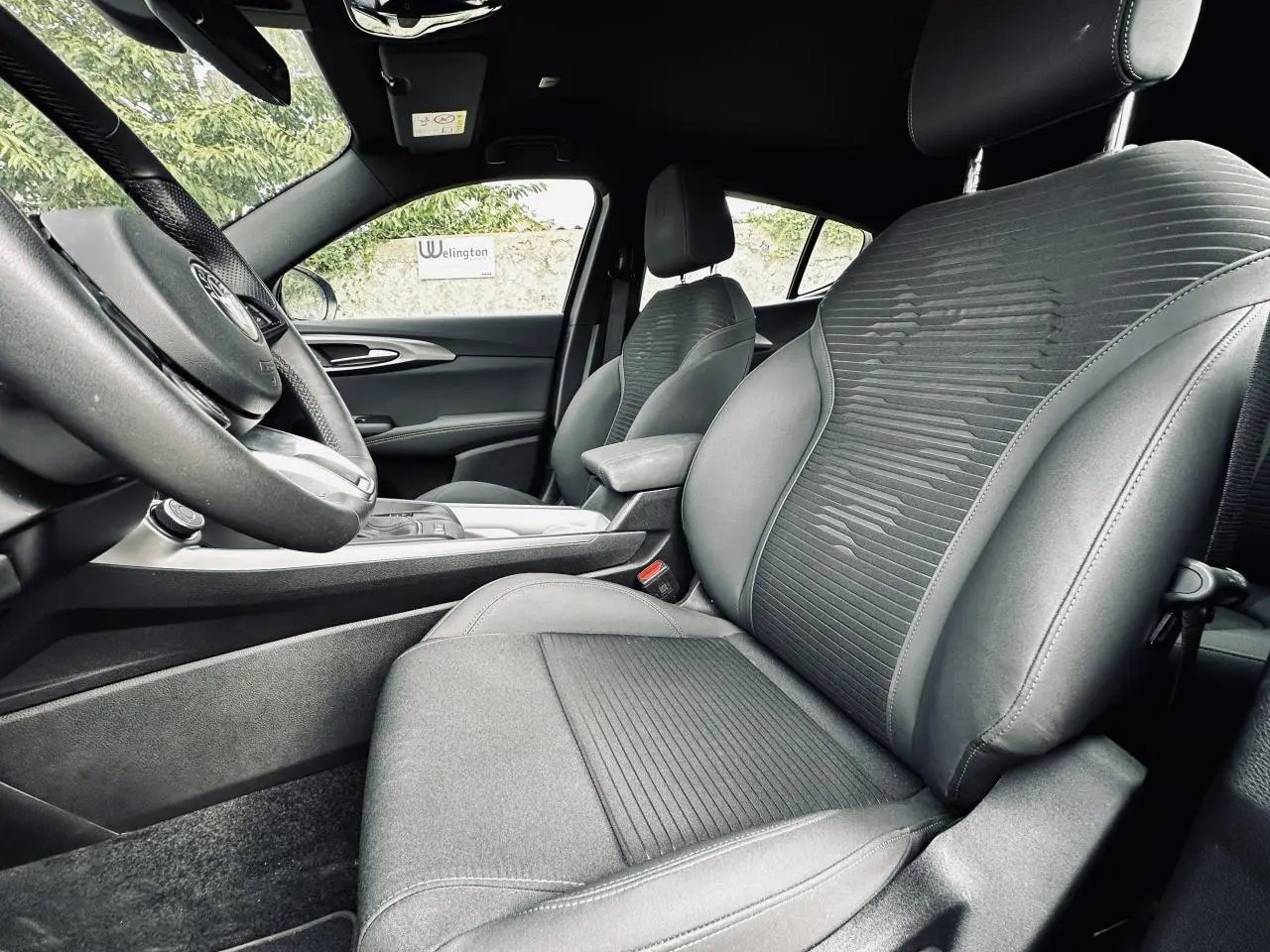 Vue intérieure côté gauche de l'Alfa Romeo Tonale 2024, sièges en cuir et tissu gris avec accoudoir central.