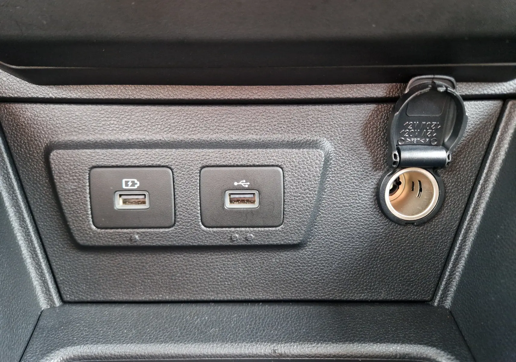Gros plan sur les ports USB et prise 12V du tableau de bord noir du Dacia Duster blanc 4x4 2022.