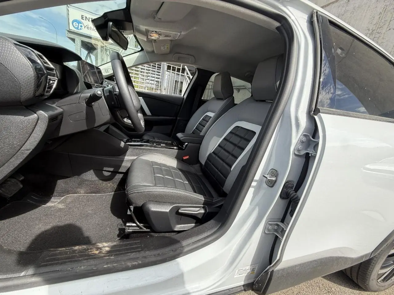 Vue intérieure côté conducteur de la Citroën C4 blanc okenite 2025, sièges bi-ton noir et gris avec console centrale visible.