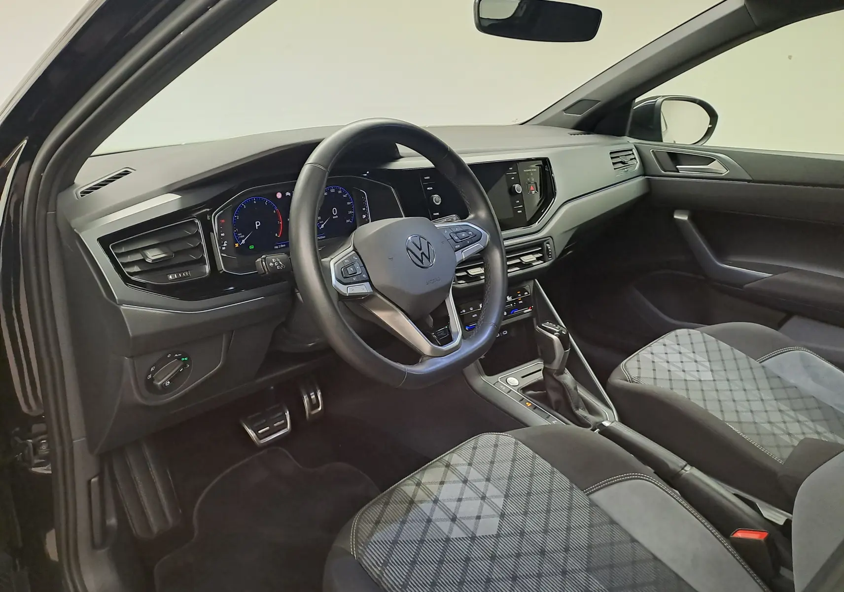 Vue intérieure côté conducteur du Volkswagen Taigo 2025 noir intense, volant multifonction et sièges tissu à motif géométrique.