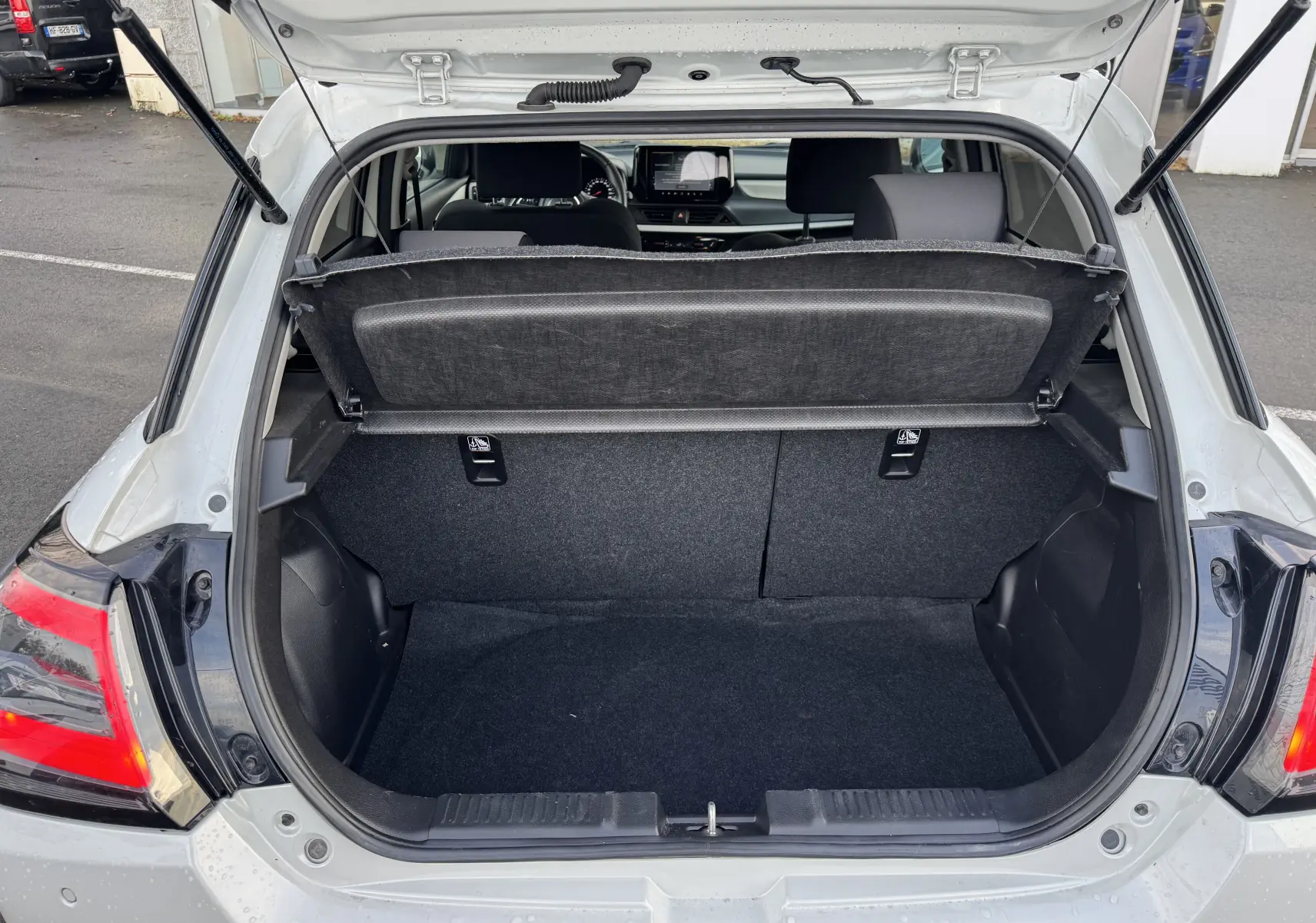 Coffre ouvert vu de l'arrière d'une Suzuki Swift blanche 2025, intérieur noir et banquette arrière visible.