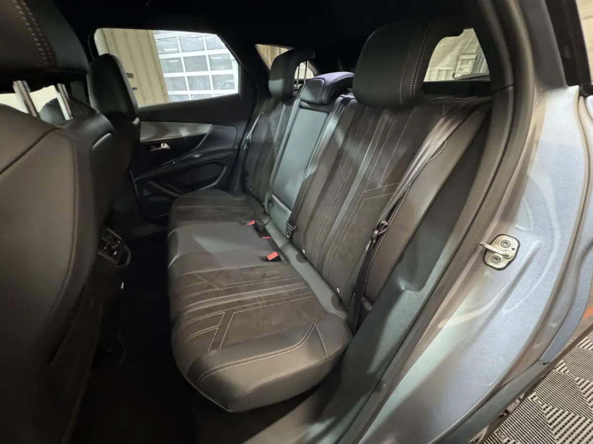 Vue intérieure côté arrière droit du Peugeot 3008 gris clair, montrant la banquette arrière en cuir noir avec surpiqûres contrastées.