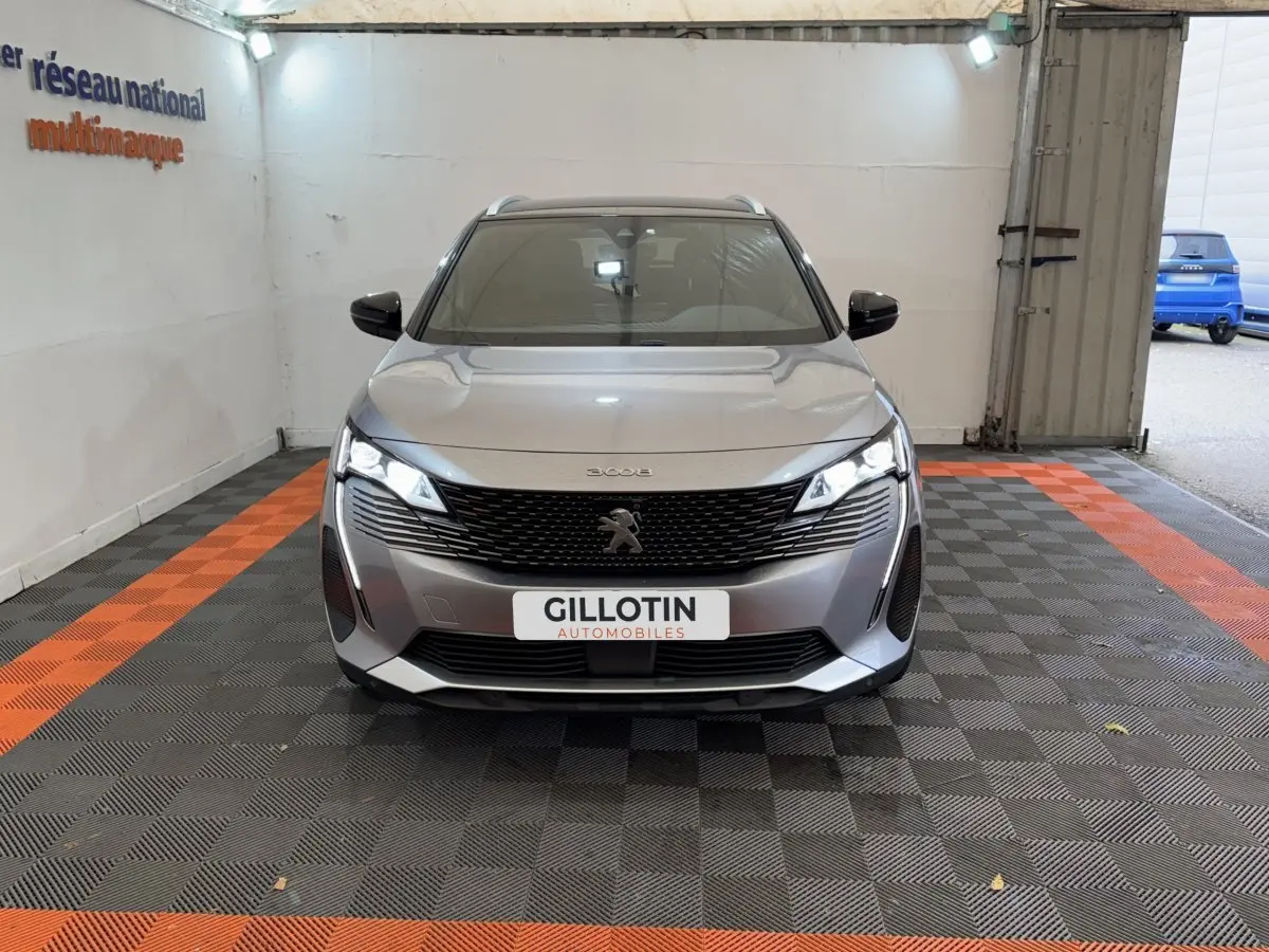 Peugeot 3008 BlueHDi 130 GT gris clair vue de face, avec calandre noire et phares LED allumés dans un garage.