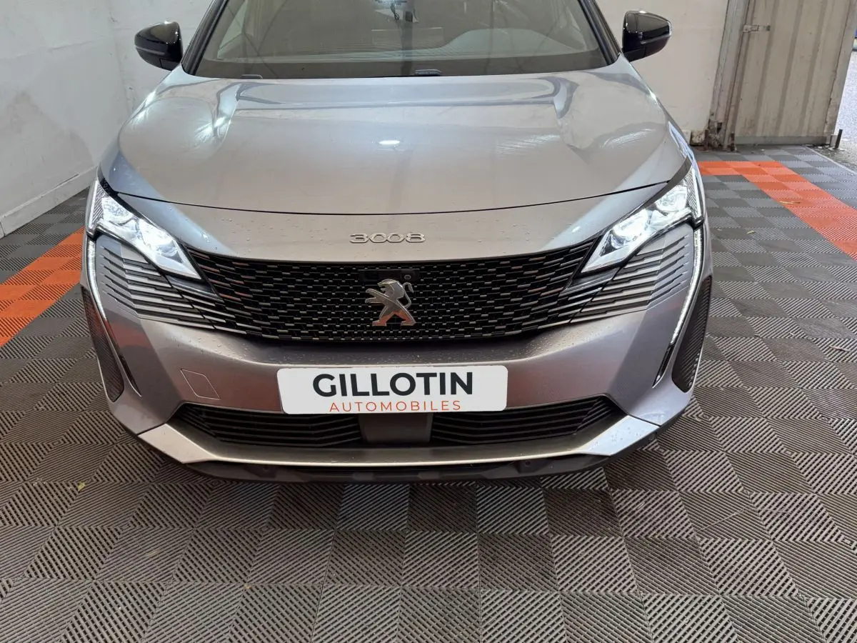 Vue frontale d'un Peugeot 3008 gris clair avec calandre noire et phares LED allumés dans un garage.