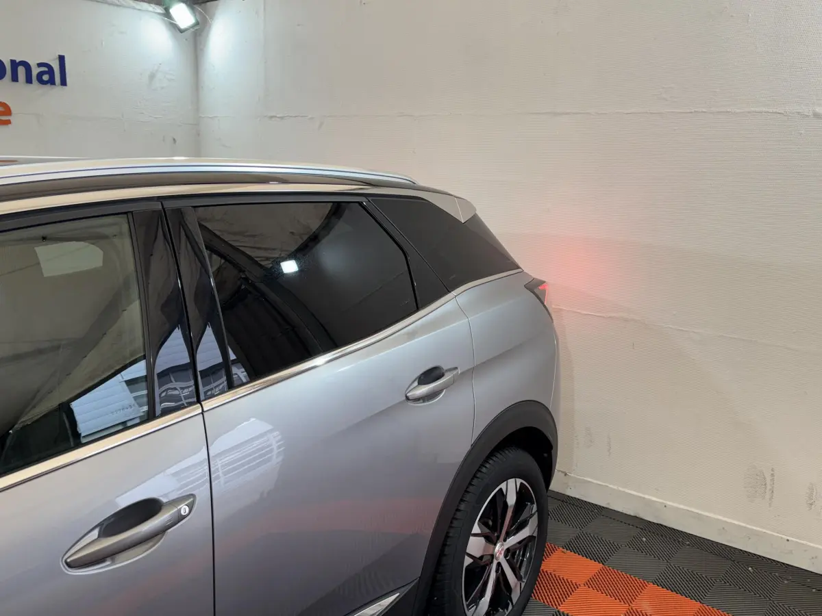 Vue côté gauche arrière d'un Peugeot 3008 gris clair avec vitres teintées et jantes alliage noires et argentées.