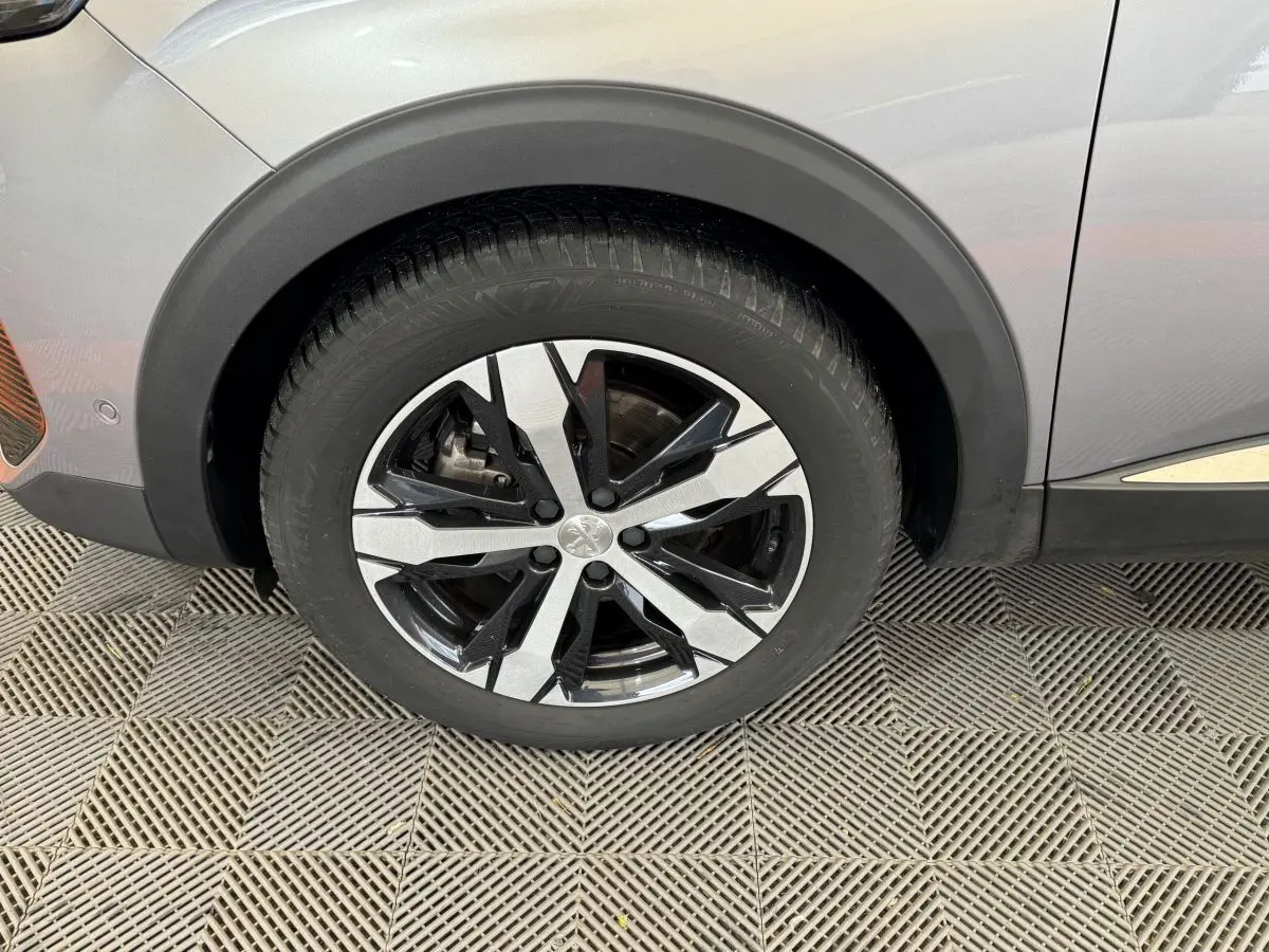 Gros plan sur la roue avant gauche du Peugeot 3008 gris clair, mettant en valeur la jante alliage bicolore au design moderne.