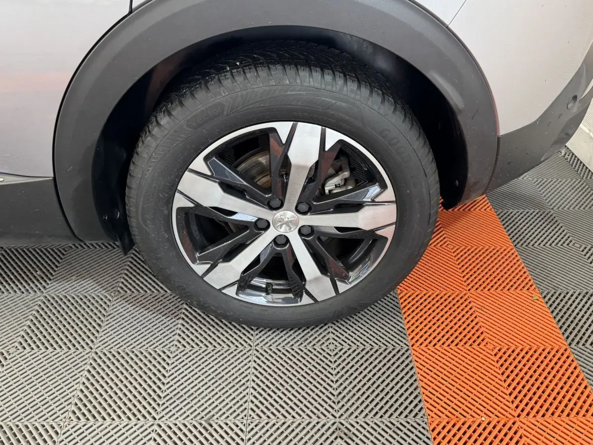 Gros plan sur la roue avant gauche d’un Peugeot 3008 gris clair avec jante alliage bicolore moderne.