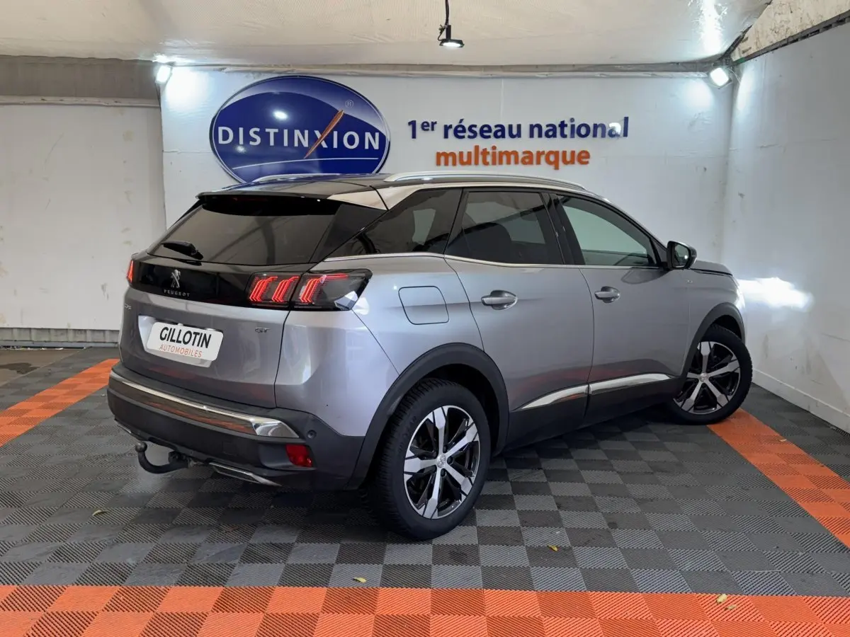 Peugeot 3008 BlueHDi 130 GT gris clair vue 3/4 arrière droit en intérieur avec toit noir et feux LED distinctifs.