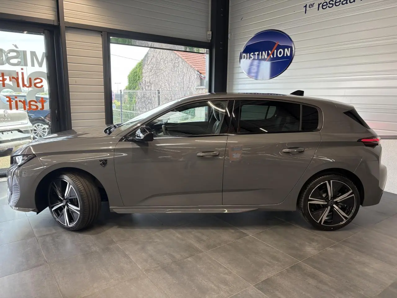 Profil droit de la Peugeot 308 GT 2025 gris selenium avec jantes alliage 18'' et vitres surteintées en showroom.