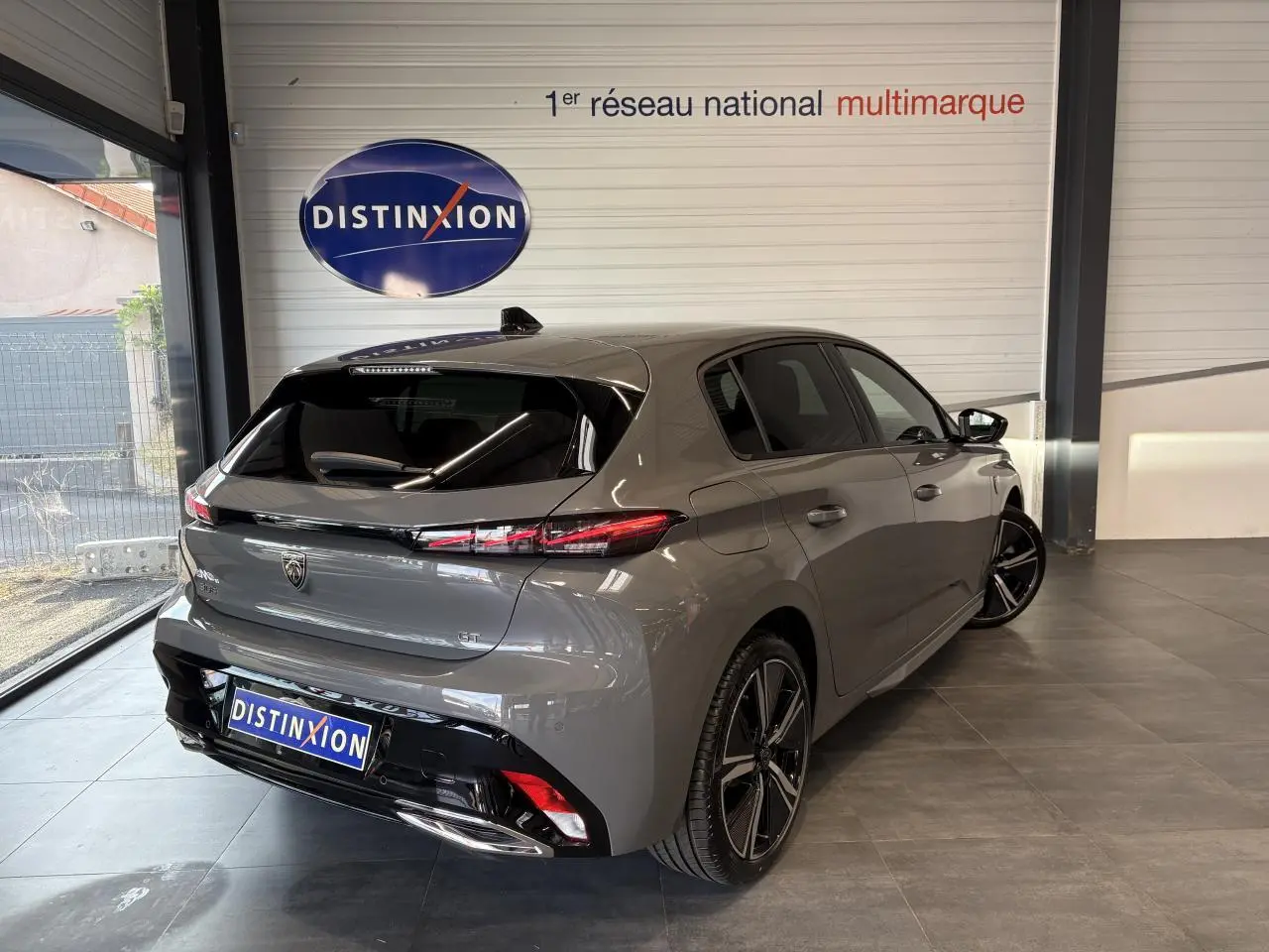 Vue 3/4 arrière droite d'une Peugeot 308 GT 2025 gris selenium avec jantes alliage 18'' et bandeau noir brillant arrière.
