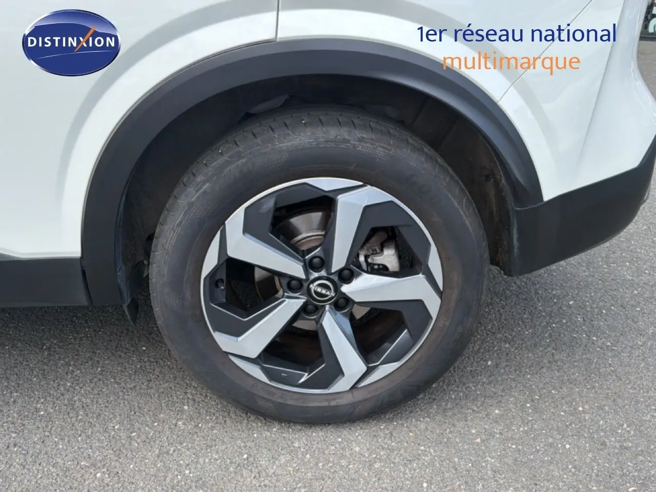 Gros plan sur la roue arrière droite du Nissan Qashqai blanc nacré, mettant en valeur la jante alliage bicolore au design moderne.