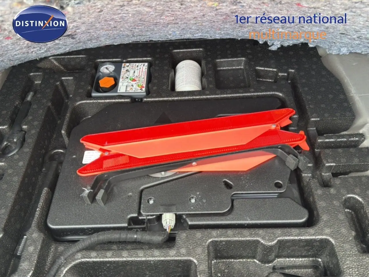 Gros plan sur le rangement sous coffre avec triangle de signalisation rouge et kit de réparation sur Nissan Qashqai blanc nacré.