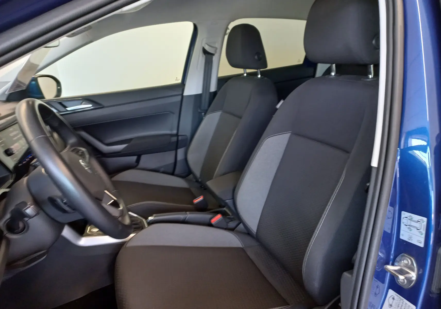 Vue intérieure côté conducteur du Volkswagen Taigo bleu récif 2025, montrant les sièges avant en tissu noir et gris.
