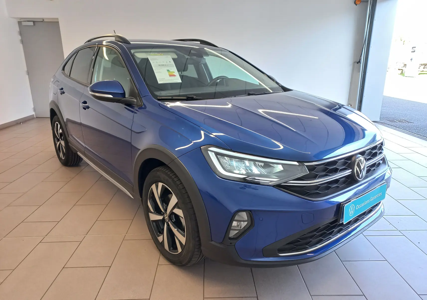 Volkswagen Taigo bleu récif en 3/4 avant droit, jantes alliage 17 pouces et calandre noire en showroom.