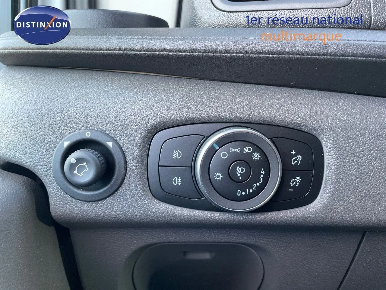 Gros plan sur le tableau de bord gris du Ford Transit Fourgon 2023 montrant les commandes d'éclairage et de réglage intérieur.