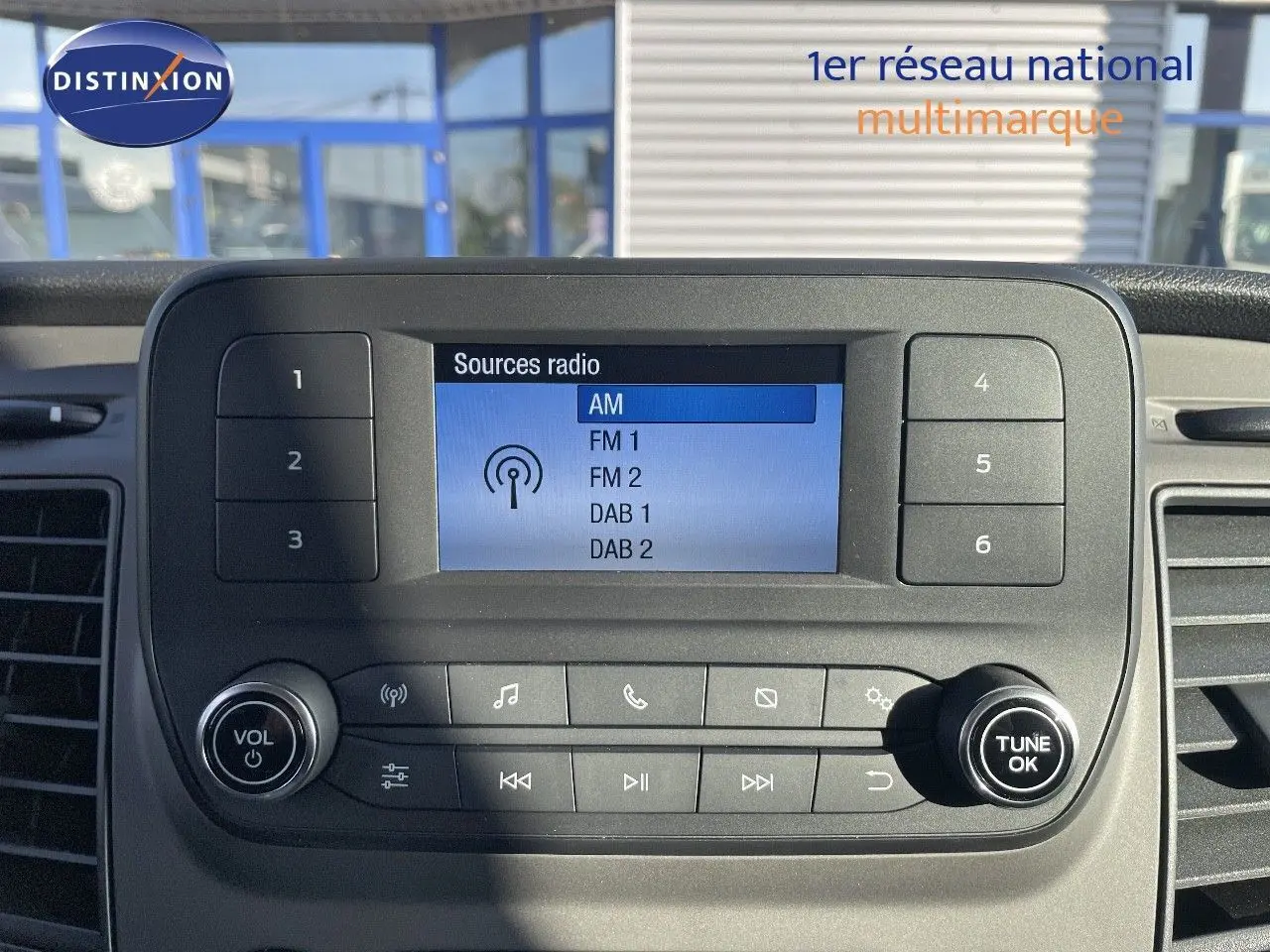 Vue rapprochée de l'écran multimédia du Ford Transit Fourgon blanc 2023 affichant les sources radio AM, FM et DAB.
