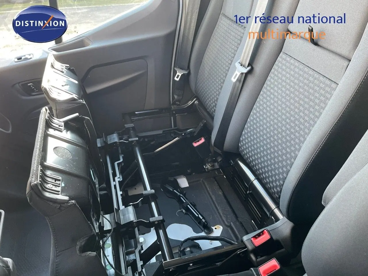 Vue intérieure du Ford Transit Fourgon 2023 montrant les sièges avant gris avec assise centrale relevée et structure métallique apparente.