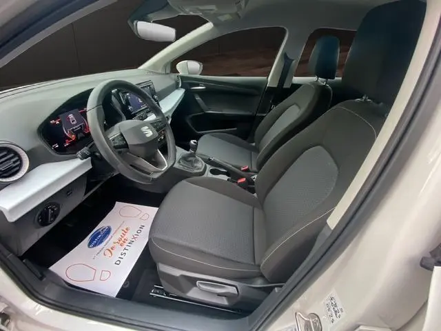 Intérieur de la SEAT IBIZA blanc candy 2023, vue côté conducteur, sièges tissu gris et tableau de bord moderne.