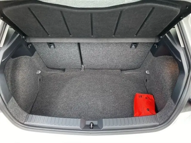 Coffre ouvert vu de l'arrière d'une SEAT Ibiza blanc candy 2023, avec tapis gris et trousse de secours rouge visible.
